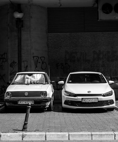grayscale photo of two Volkswagen cars parked on sidewalk
