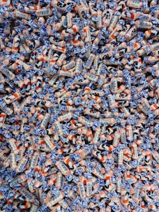 A large pile of colorful candies wrapped in white, blue, and orange packaging. The candies have illustrations and text on them, showcasing a playful and vibrant design.