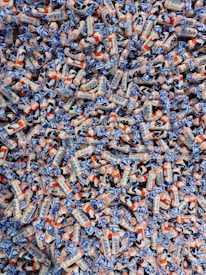 A large pile of colorful candies wrapped in white, blue, and orange packaging. The candies have illustrations and text on them, showcasing a playful and vibrant design.