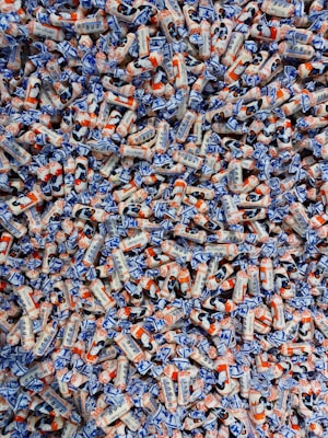 A large pile of colorful candies wrapped in white, blue, and orange packaging. The candies have illustrations and text on them, showcasing a playful and vibrant design.