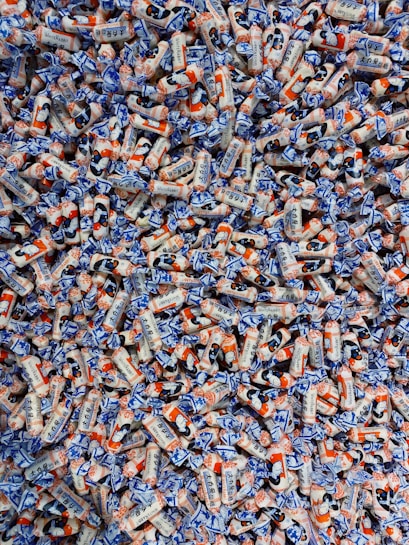 A large pile of colorful candies wrapped in white, blue, and orange packaging. The candies have illustrations and text on them, showcasing a playful and vibrant design.