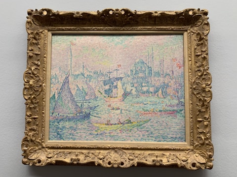 A colorful pointillist painting depicts boats on water with a city skyline in the background. The scene is filled with vibrant dots of color, creating a textured and dynamic effect. Sailboats with varying sail shapes and sizes can be seen on the water, and a bustling cityscape is visible in the distance.