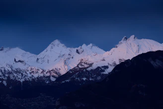 A high-resolution photo capturing the soft pink light of sunrise on sharp, icy mountain peaks.