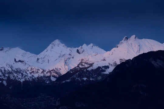 A high-resolution photo capturing the soft pink light of sunrise on sharp, icy mountain peaks.