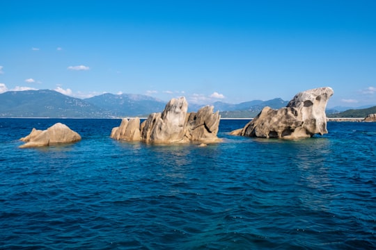 brown rock formations near body of water viewing mountain under blue and white sky in Korsika France