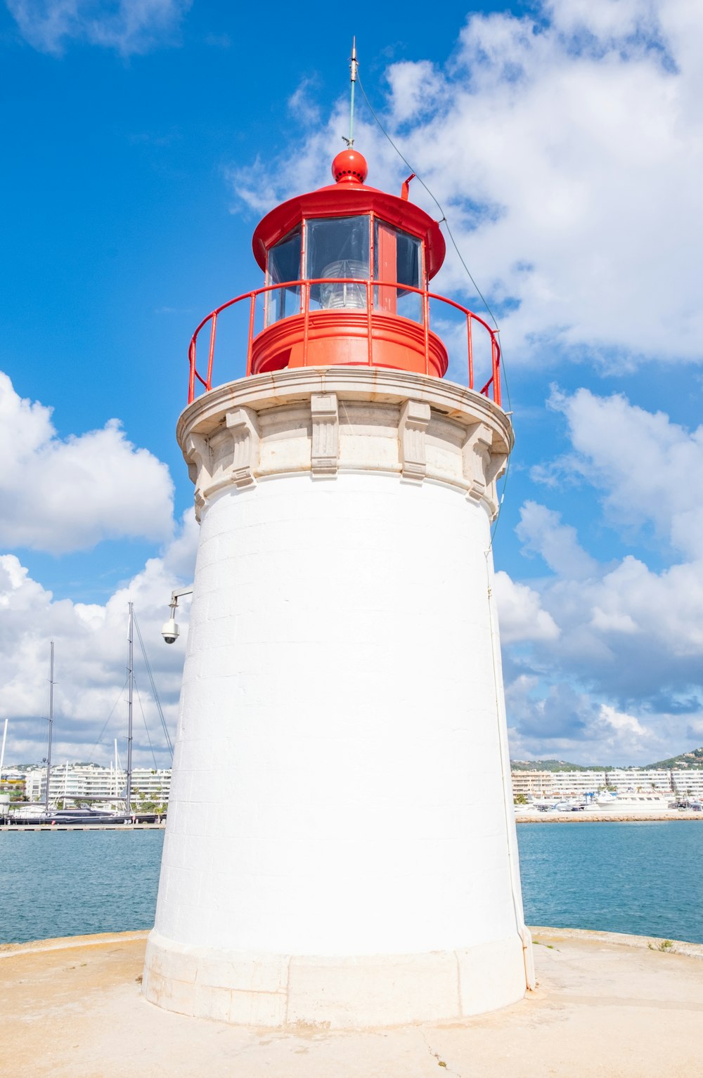 white and red lighthouse near body of water under white and blue sky