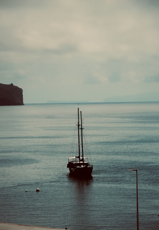 black boat on body of water viewing cliff under white and blue sky in Funchal Portugal