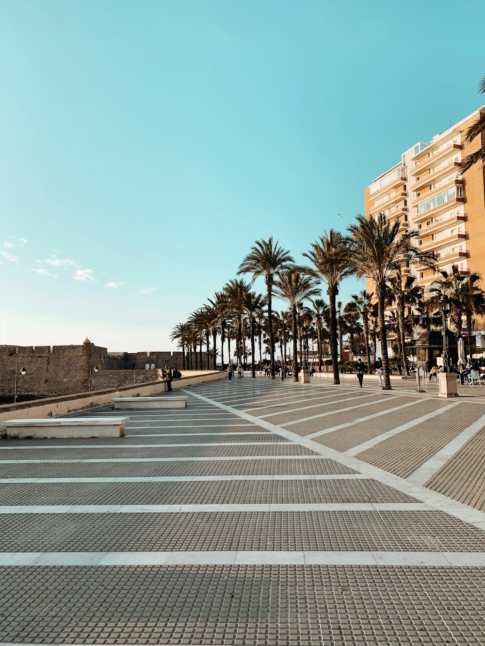 people standing on pathway near brown buildings under blue and white sky