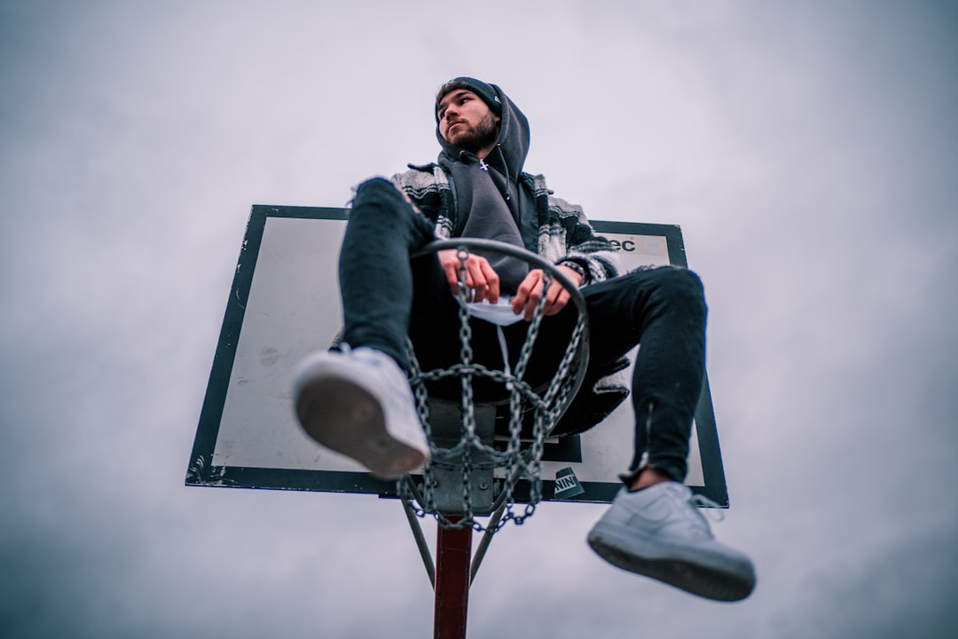 man sitting on basketball hoop during day
