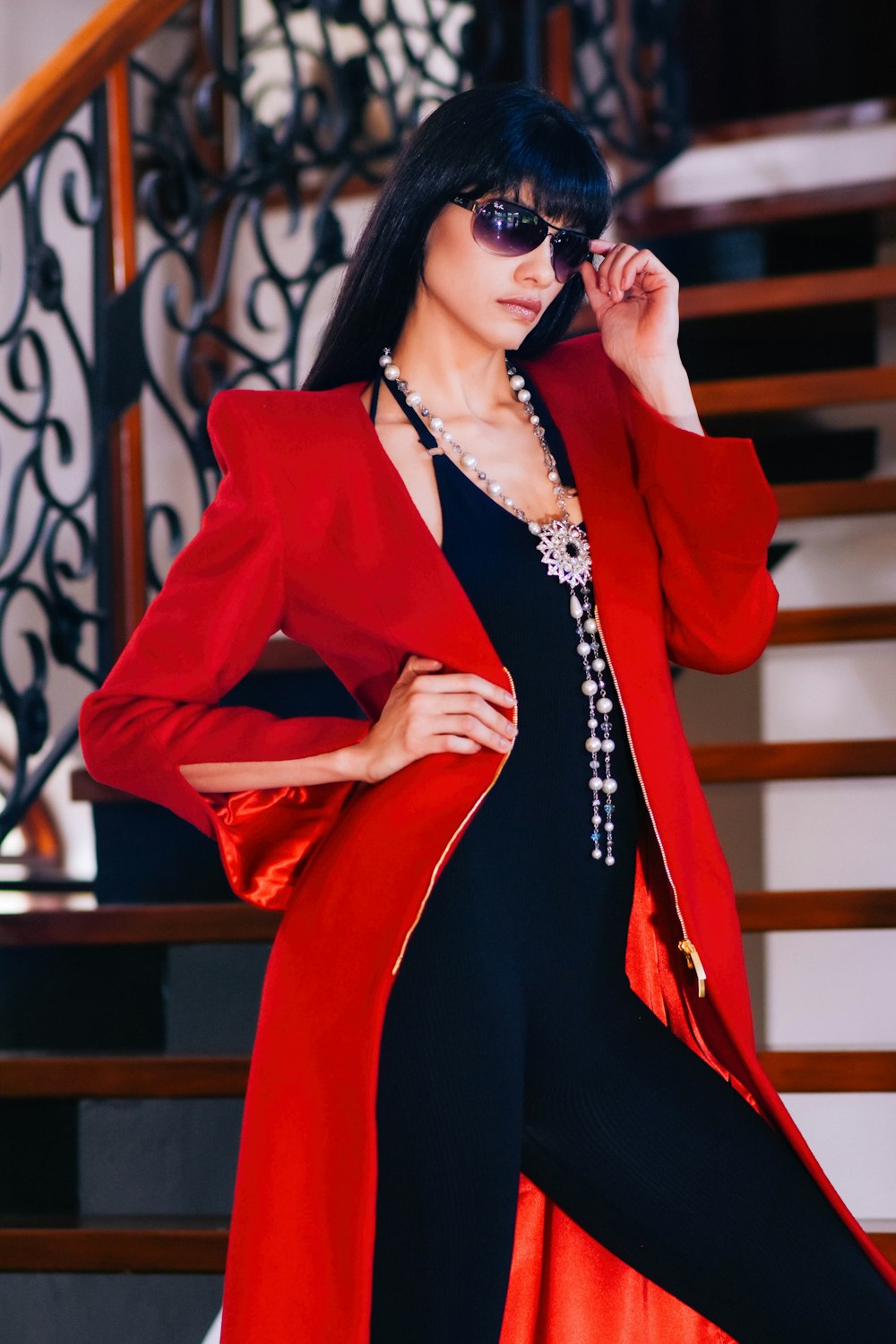 woman wearing red coat and sunglasses standing with right arm akimbo