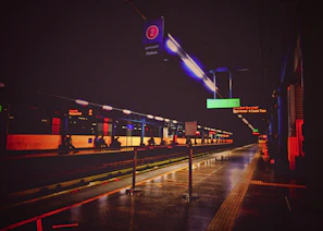 A bright LED billboard glowing at dusk on a bustling railway station platform.