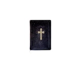 A black book with a gold cross on its cover is centered against a plain, white background. The book appears to have a textured surface, and the cross design is simple and prominent.