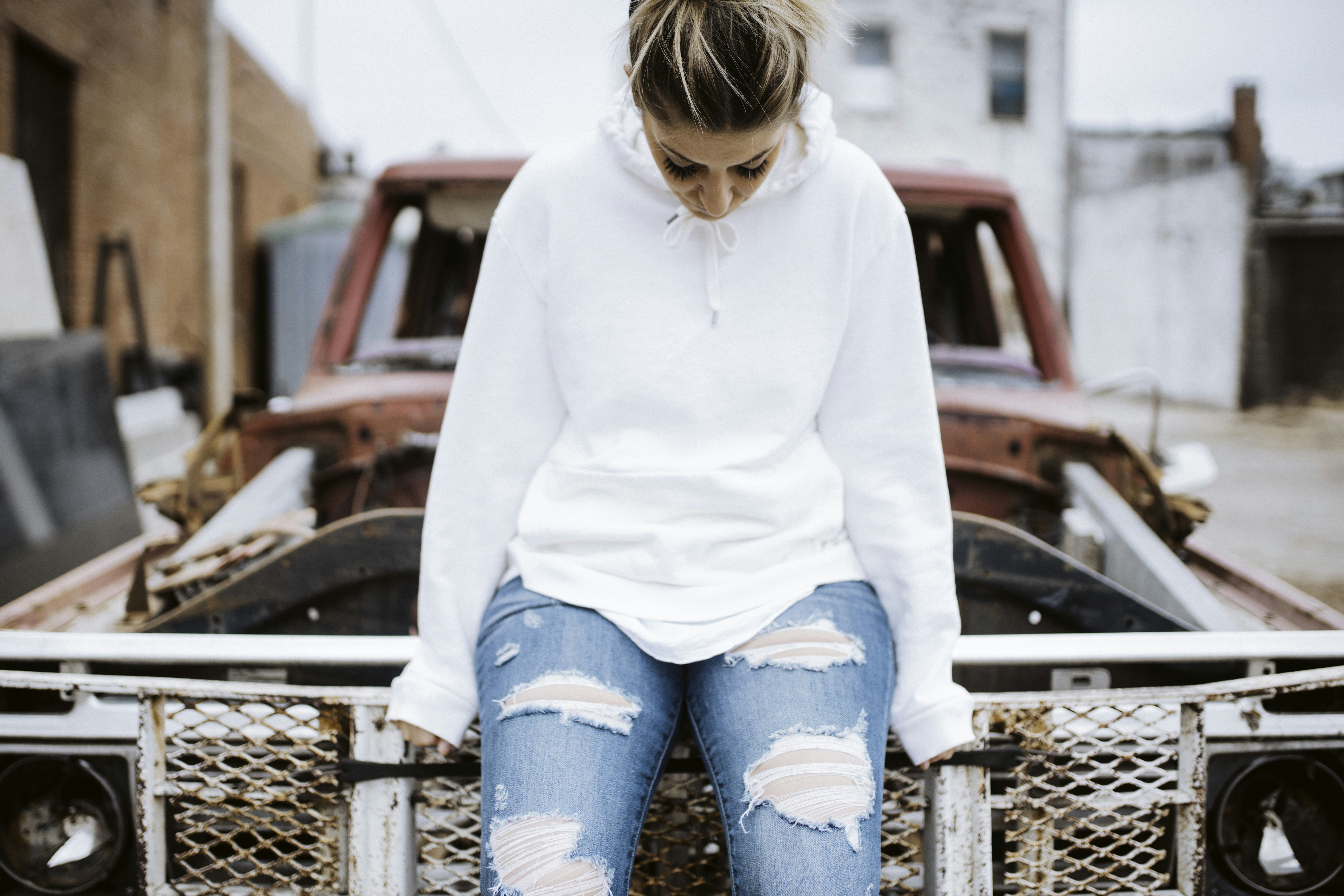 woman in jeans and sweater sitting on top of hood of vehicle at daytime kansas teams background