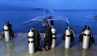 A sturdy scuba tank standing upright on a rocky shore at sunset