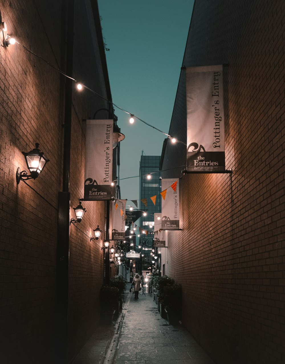 person walking on street between buildings with string light on toabove