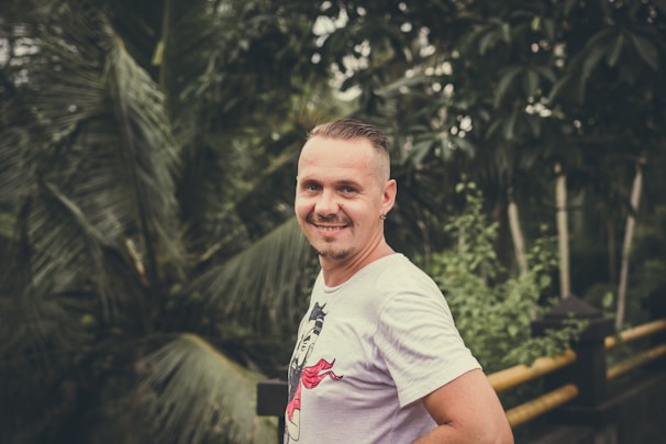 A man with healthy, shiny hair smiling confidently outdoors surrounded by greenery