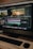 A computer monitor displays a video editing software interface with several video clips and sequences being edited. The workspace includes timelines, video previews, and various tools. Below the monitor are a keyboard and a mouse on a wooden desk.