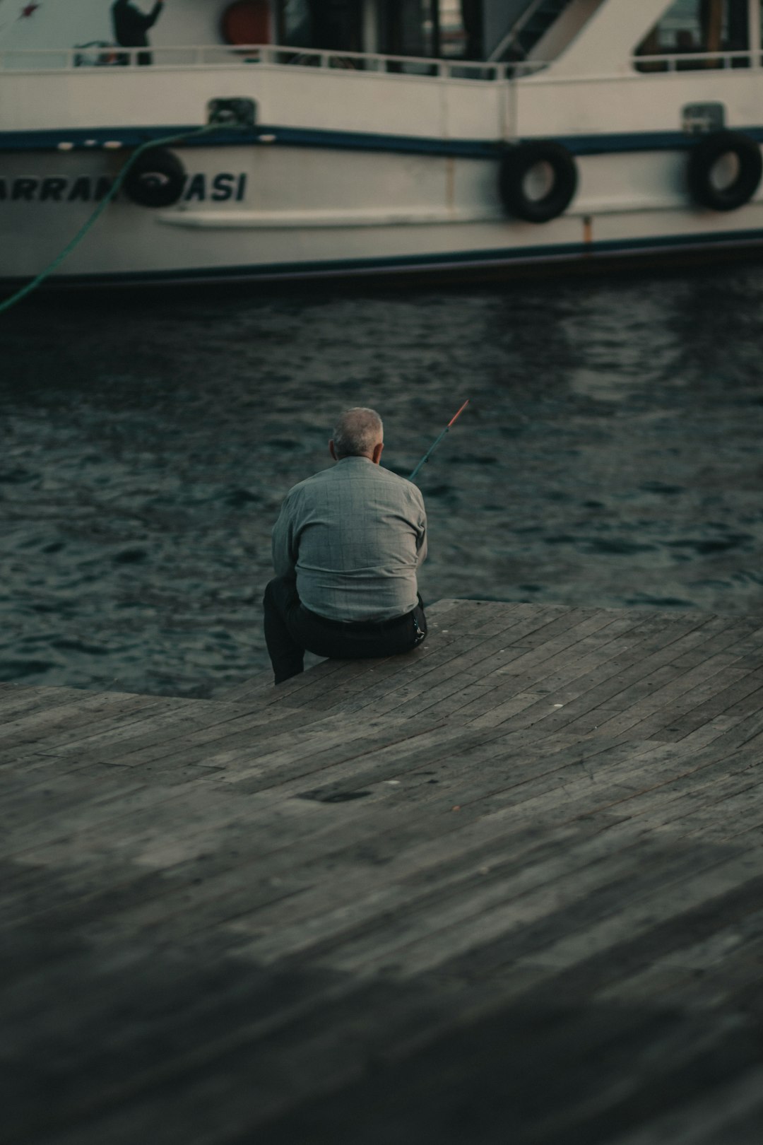 man sitting and fishing near boat during day