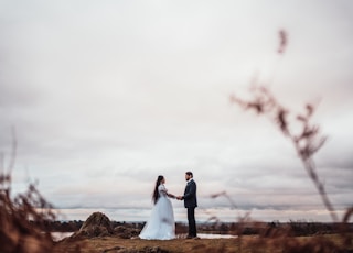 couple in wedding attires holding hands by rock under white skiews during daytime