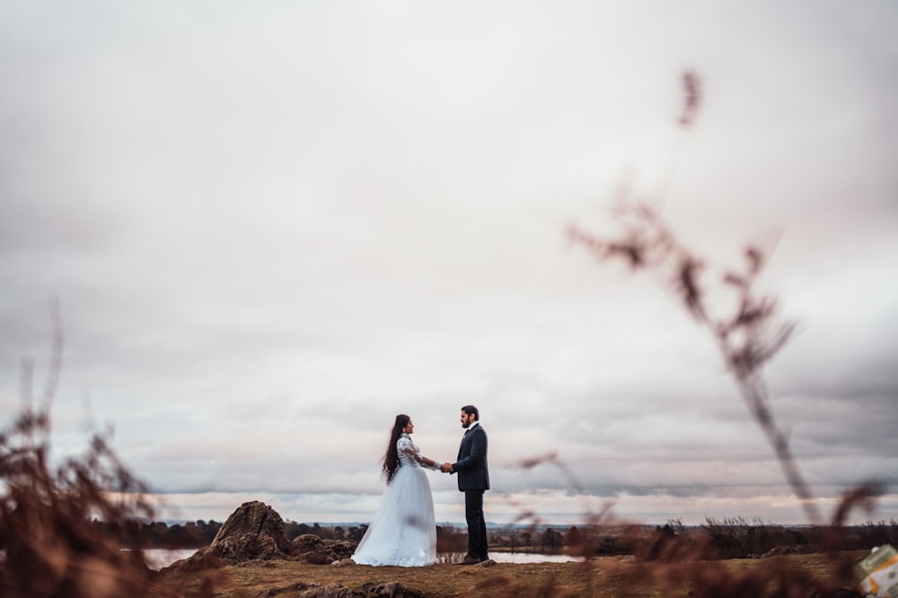 couple in wedding attires holding hands by rock under white skiews during daytime