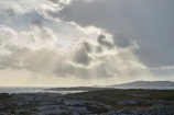 Sunlight breaking through clouds over a rugged coastline, highlighting textures.