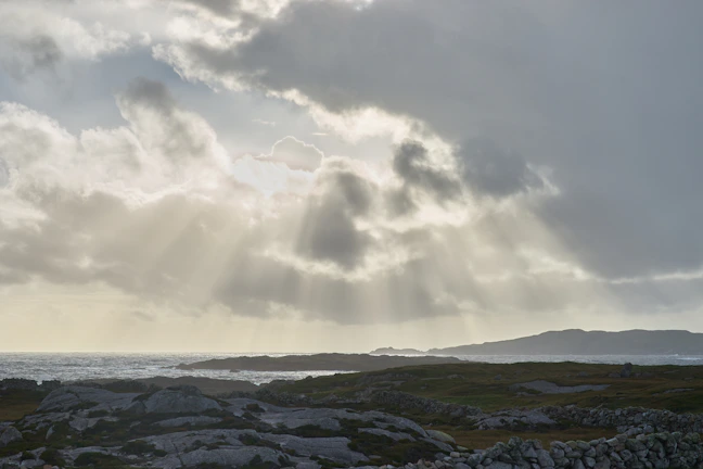 Sunlight breaking through clouds over a rugged coastline, highlighting textures.