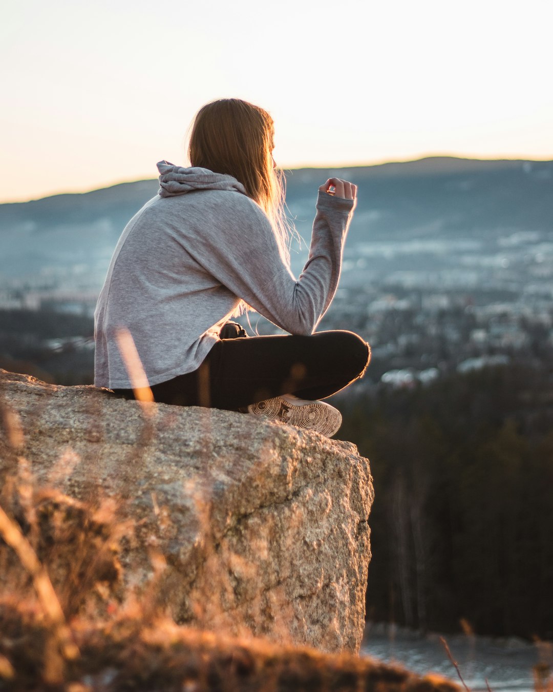 woman wearing grey hooded jacket sitting on the stone