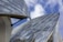 Modern architectural structures with large, curved glass panels against a blue sky with white clouds. The buildings appear to have a sleek, futuristic design with reflective surfaces and metallic support elements.