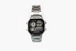 A silver digital wristwatch with a rectangular face displaying the time, world time map, and additional features. The watch has a metal strap and a robust, classic design.