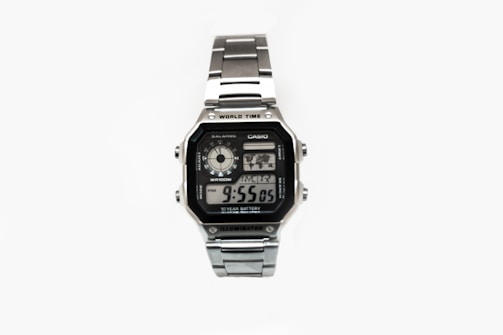 A silver digital wristwatch with a rectangular face displaying the time, world time map, and additional features. The watch has a metal strap and a robust, classic design.
