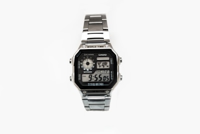 A silver digital wristwatch with a rectangular face displaying the time, world time map, and additional features. The watch has a metal strap and a robust, classic design.