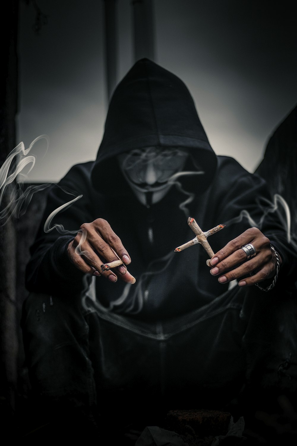 person in Guy Fawkes mask holding cross-shaped lighted cigarettes on his left with lighted joice on right hand