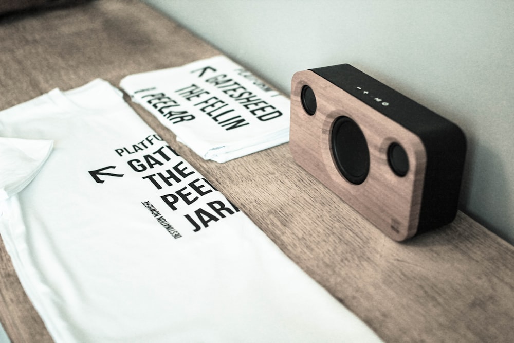 two white crew-neck shirts beside a black and brown portable wireless speaker