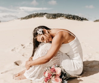 woman in white spaghetti strap dress sitting on sand