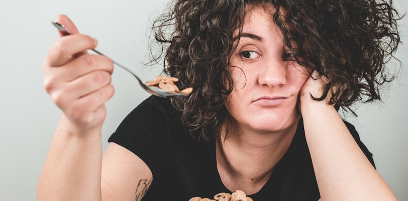 woman with messy hair wearing black crew-neck t-shirt holding spoon with cereals on top