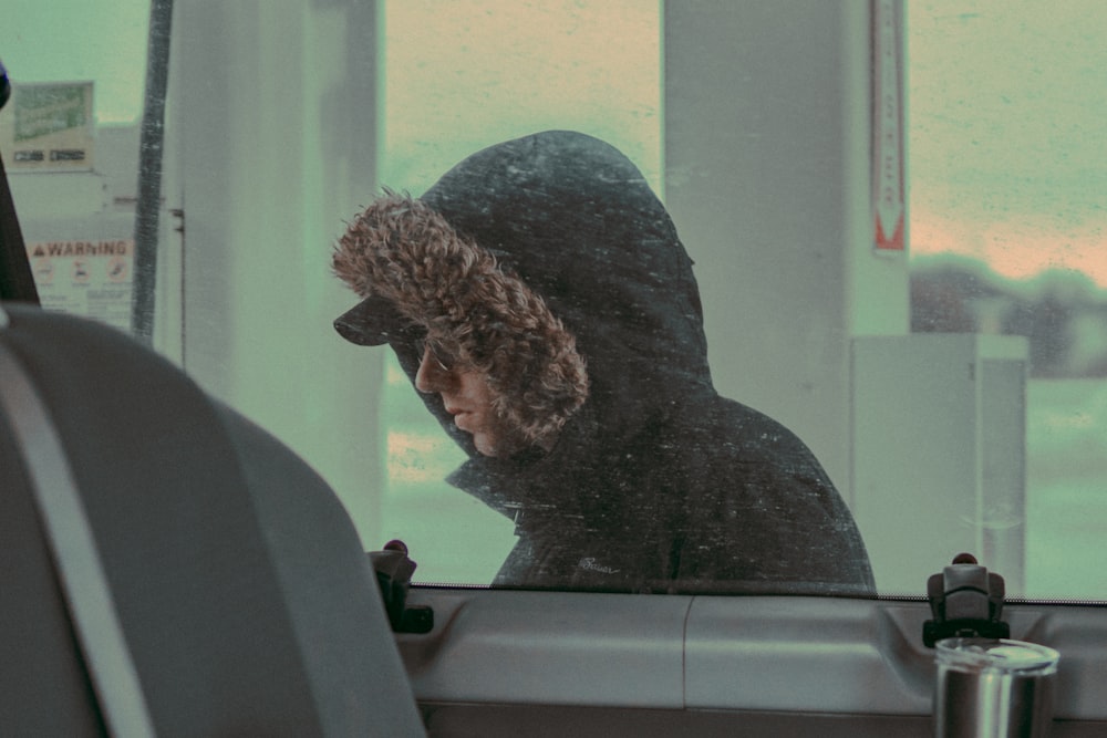 person in brown and black fur-trimmed hooded jacket through glass vehicle window