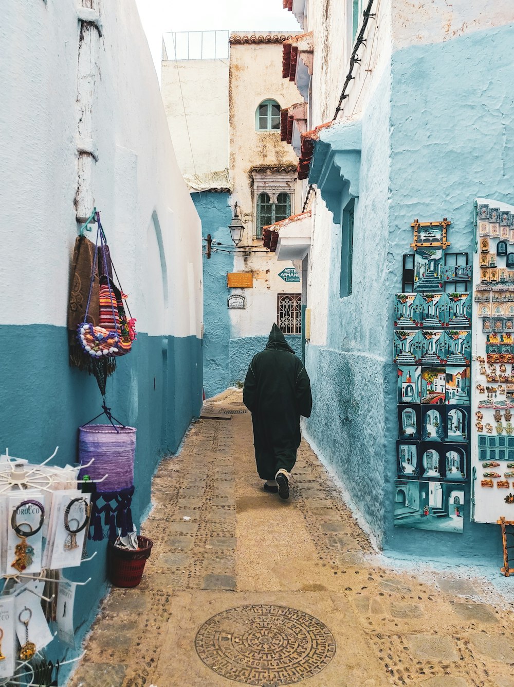 person wearing hooded jacket walking on alley between buildings during daytime