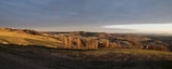 A wide landscape shot of rolling hills under a dramatic cloudy sky at sunset.