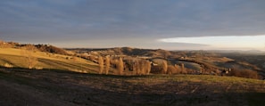 A wide landscape shot of rolling hills under a dramatic cloudy sky at sunset.