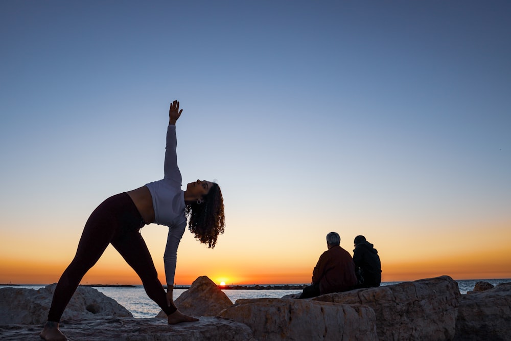 meditating woman on top of rock by 2 person by body of water