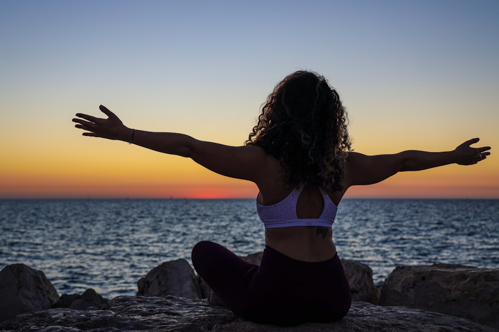 woman wearing sports bra sitting in front of the ocean