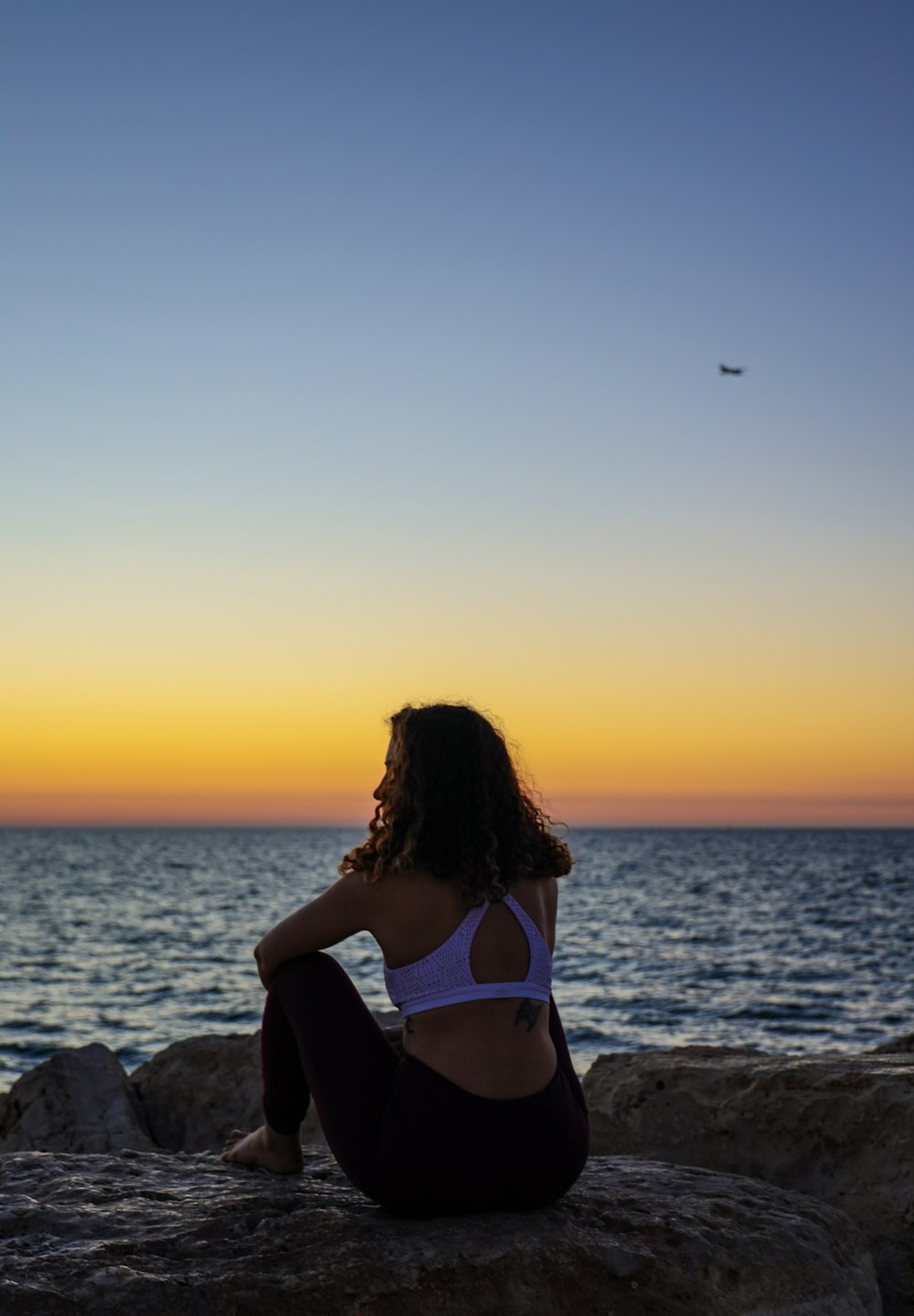 Mujer sentada en una roca frente al mar durante la hora dorada