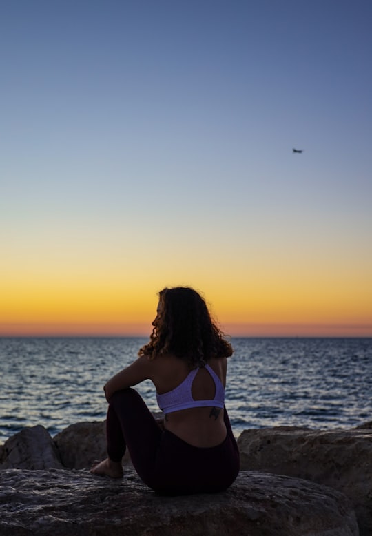 woman sitting on a rock facing the sea during golden hour in Tel Aviv Port Israel
