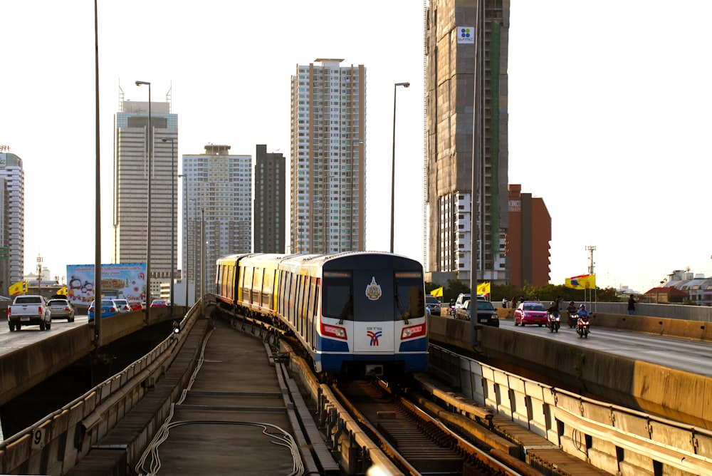 white and blue train on railway and other vehicles on road near buildings during daytime