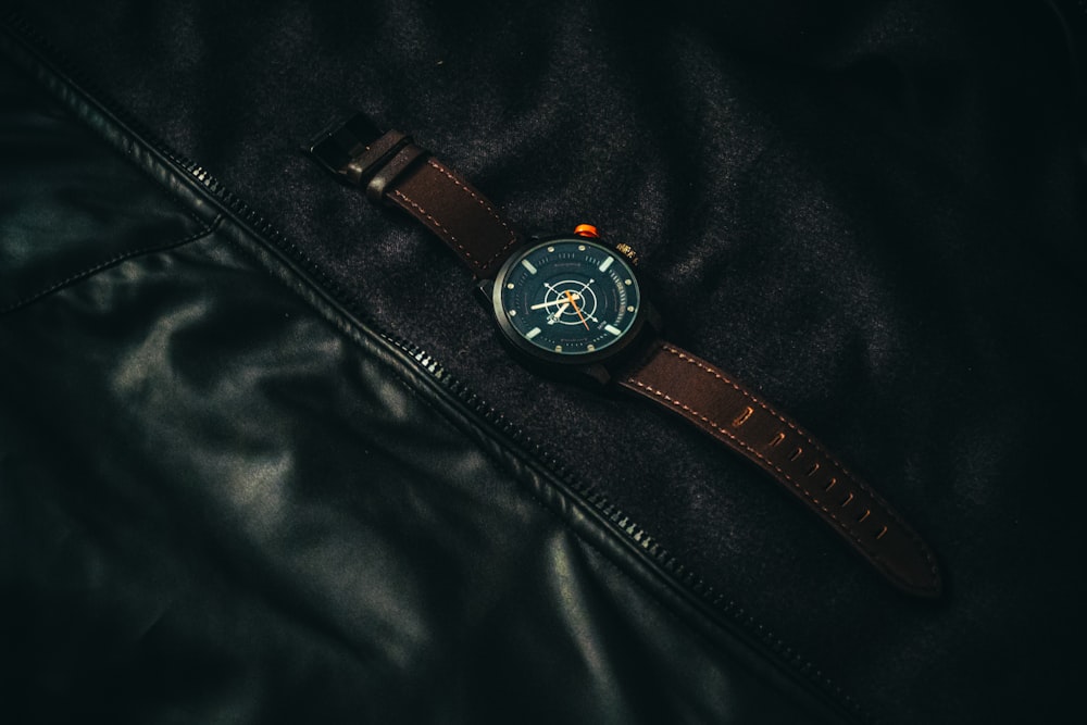 round black analog watch with brown leather band on black leather apparel