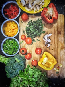 orange tomatoes near sliced yellow bell pepper, broccoli on wooden chopping board