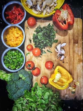 orange tomatoes near sliced yellow bell pepper, broccoli on wooden chopping board