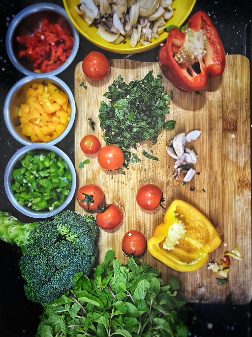 pomodori arancioni vicino peperone giallo a fette, broccoli su tagliere di legno