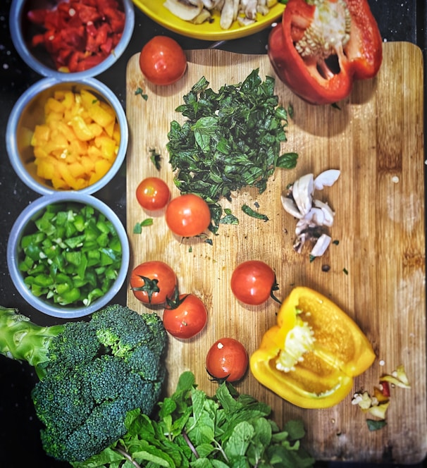 orange tomatoes near sliced yellow bell pepper, broccoli on wooden chopping board