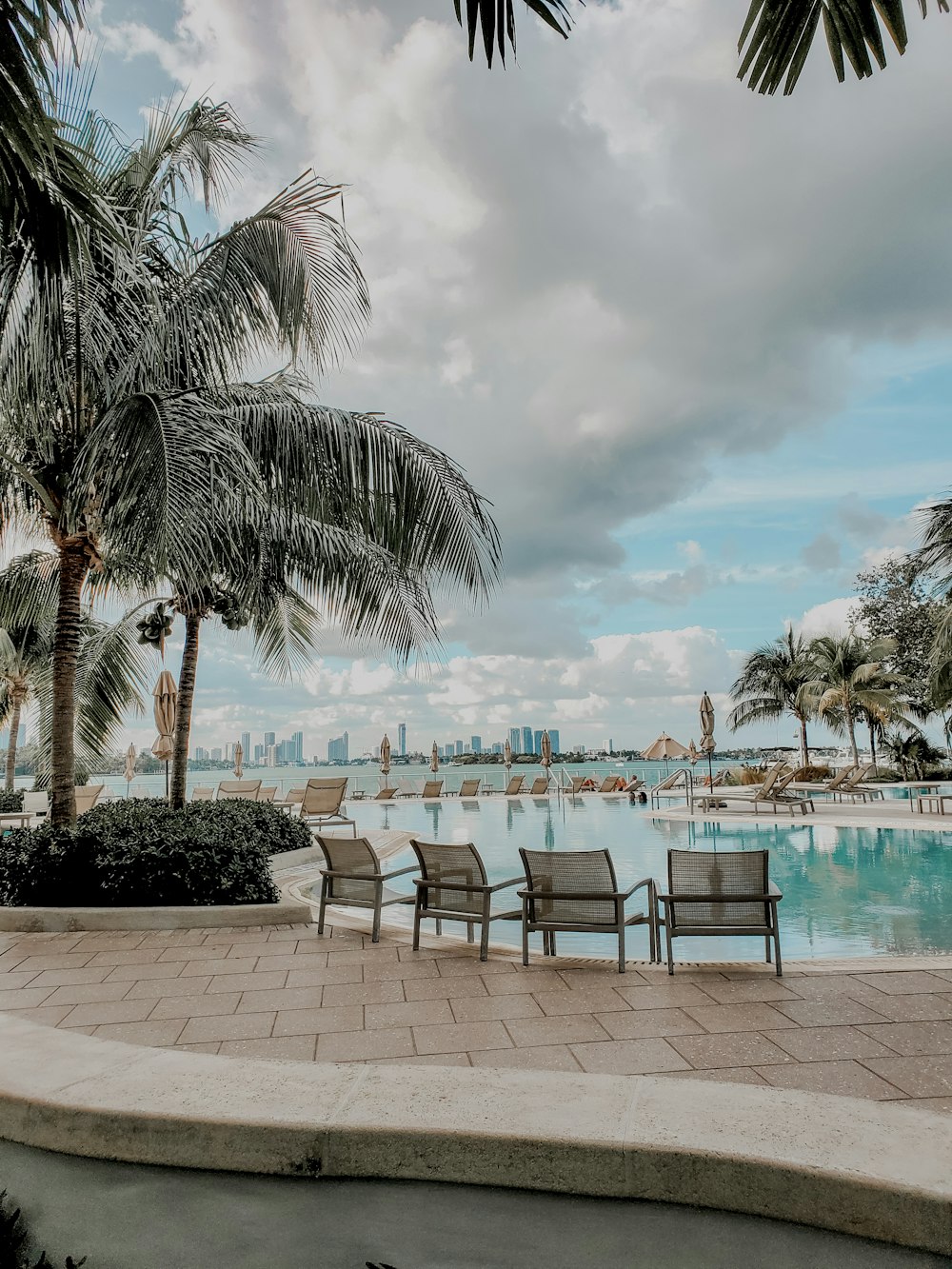 four gray pool chairs near sea-side swimming pool viewing blue sea under white and blue sky